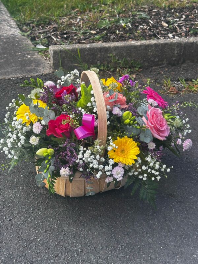 Bright Delight - A vibrant, hand-arranged basket that captures the warmth and charm of a blooming garden. Featuring a lively mix of bright and soft hues, this piece is thoughtfully styled with lush greenery, delicate fillers, and eye-catching focal blooms, all nestled in a rustic wooden basket with a curved handle. Accented with a cheerful ribbon, it’s perfect for celebrations, heartfelt gifts, or simply brightening someone’s day with a touch of natural elegance.