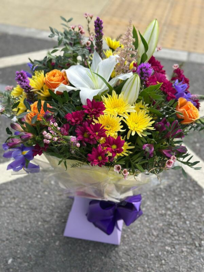 Vibrant Garden - A lively and eye-catching bouquet bursting with rich color and fresh energy. Featuring a dynamic mix of bold yellows, deep pinks, vivid purples, and warm orange tones, this arrangement creates a striking and joyful display. Lush greenery and delicate accents add texture and movement, while the elegant wrap and coordinating ribbon give it a polished finish. Perfect for celebrations, special occasions, or sending a bright and uplifting gesture.