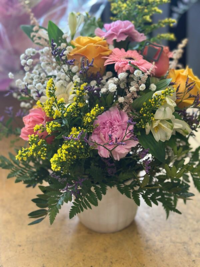 Wild Garden - A lush and expressive arrangement inspired by the beauty of a blooming countryside garden. Featuring a vibrant mix of soft pinks, warm peach tones, creamy whites, and sunny yellow accents, this design is full of natural movement and texture. Delicate filler elements and rich greenery create depth and a slightly untamed, organic feel. Presented in a simple, elegant container, it’s perfect for gifting, celebrations, or bringing a fresh, joyful touch to any space.