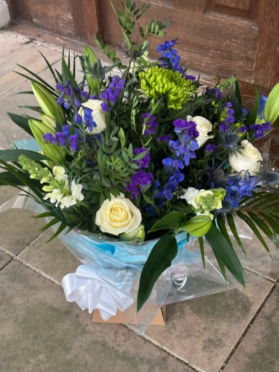 Bluebell Twilight - A striking bouquet designed with deep blue and rich violet tones, softened by creamy whites and fresh green accents. The layered greenery and textured details give it a natural, garden-inspired feel, while the crisp wrapping and white bow add a polished finishing touch. Perfect for birthdays, thoughtful gifts, celebrations, or sending a calm and elegant gesture.
