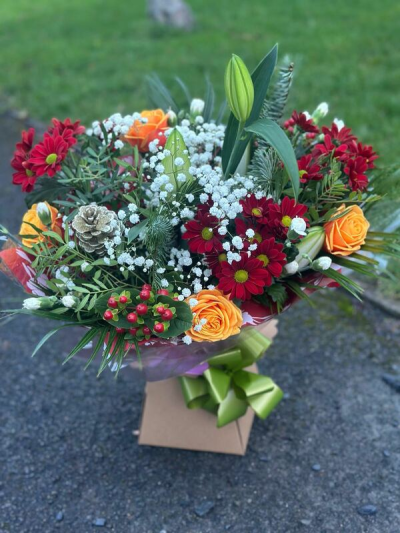 Woodland Glow - A rich and seasonal bouquet blending deep crimson tones with warm orange accents, crisp whites, and fresh greenery. Textural details and natural elements add depth and a subtle woodland charm, creating a full, lively design with plenty of movement. Finished with elegant wrapping and a coordinating bow, this arrangement is perfect for celebrations, winter occasions, or sending a warm and joyful gift.