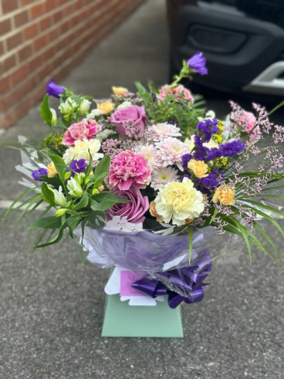 Sugar Plum - A soft and cheerful bouquet filled with a harmonious blend of pastel pinks, gentle yellows, creamy whites, and touches of lavender. Designed in a relaxed, garden-inspired style, it features a variety of textures and flowing greenery that create a light, airy feel. Finished with elegant wrapping and a coordinating ribbon, this arrangement is perfect for celebrations, thoughtful gifts, or adding a touch of delicate beauty to any setting.