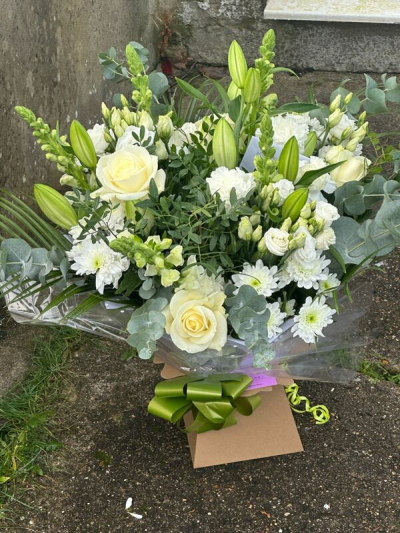 Simply Elegant - A refined and timeless bouquet showcasing a serene palette of soft ivory tones complemented by fresh green foliage. Designed in a natural, garden-inspired style, it features graceful height, gentle movement, and a beautiful mix of textures. Subtle accents add depth while maintaining a clean and calming look. Finished with elegant wrapping and a coordinating ribbon, this arrangement is perfect for sympathy gestures, weddings, or any occasion calling for understated sophistication.