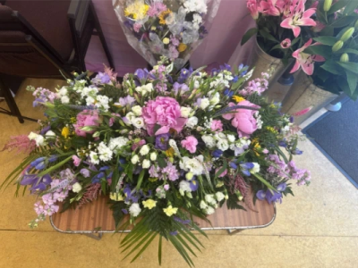 Pink Oasis Spray - A lush and abundant tribute arrangement designed in a flowing, natural style with soft pastel tones of pink, lavender, cream, and gentle greenery. Rich in texture and movement, this piece creates a serene and uplifting presence, with layers of delicate accents adding depth and grace. Its elongated form makes it ideal for memorial services or as a casket tribute, offering a beautiful expression of love, remembrance, and peaceful farewell.