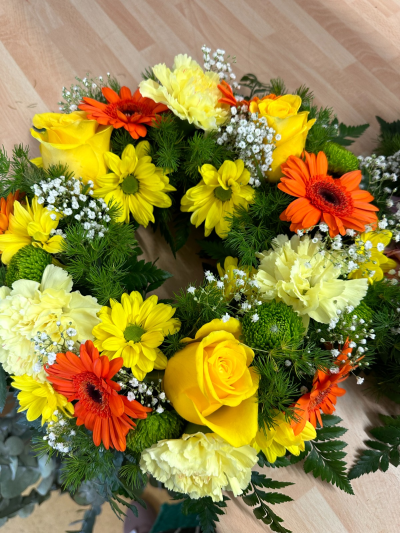 Vibrant wreath - A vibrant and uplifting circular tribute designed to celebrate a life filled with warmth and joy. Bursting with sunny yellows and rich golden-orange tones, this wreath radiates positivity and light, beautifully balanced with fresh greenery and soft, delicate accents. Its classic circular form symbolises eternity and enduring love, while the lively colour palette offers a heartfelt expression of cherished memories and bright spirits. A meaningful and comforting choice for honouring someone who brought sunshine to others.
