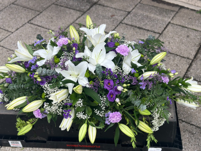Serenity Garden Tribute - A graceful and calming arrangement designed in a classic elongated style, blending soft ivory tones with gentle lilac and fresh greenery. This elegant piece evokes peace, purity, and quiet reflection, with flowing lines and delicate textures throughout. Thoughtfully arranged to create a natural, garden-inspired feel, it offers a beautiful and heartfelt way to honour a loved one with dignity and tranquillity.