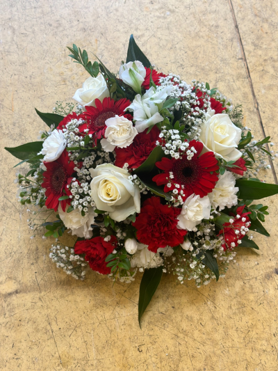 Posy in oasis - A classic and elegant posy arrangement featuring a harmonious blend of rich crimson and soft ivory tones, beautifully complemented by fresh greenery. Carefully designed in a rounded style, this piece conveys love, respect, and enduring remembrance. The contrast of bold and gentle hues creates a striking yet balanced tribute, making it a heartfelt choice for honouring a cherished life with grace and dignity.